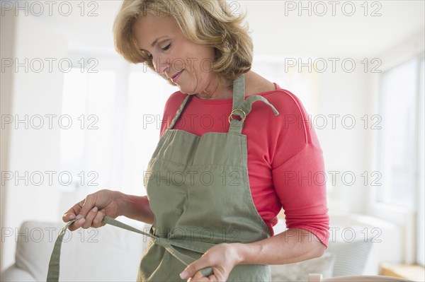 Caucasian woman tying apron in living room
