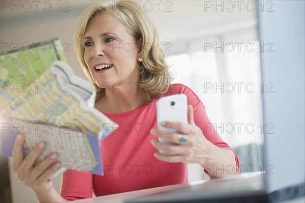 Caucasian woman using roadmap and cell phone to plan trip