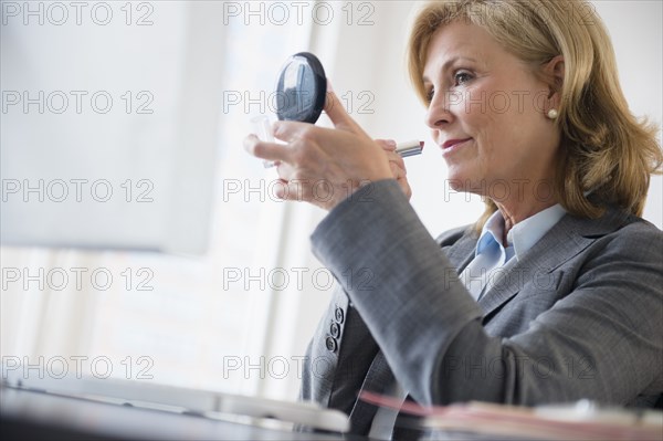 Caucasian businesswoman applying makeup in office