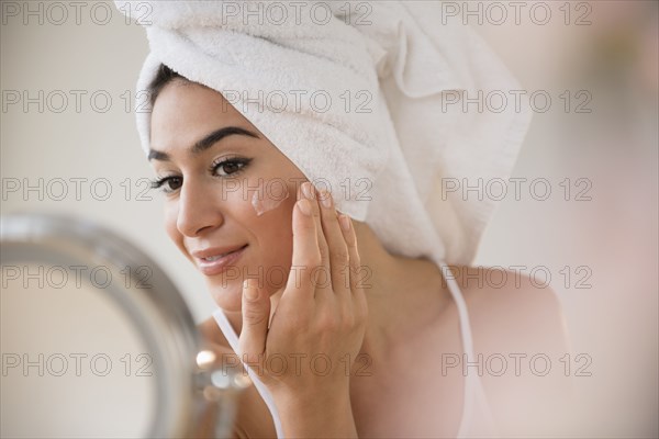 Woman with hair in towel rubbing lotion on face