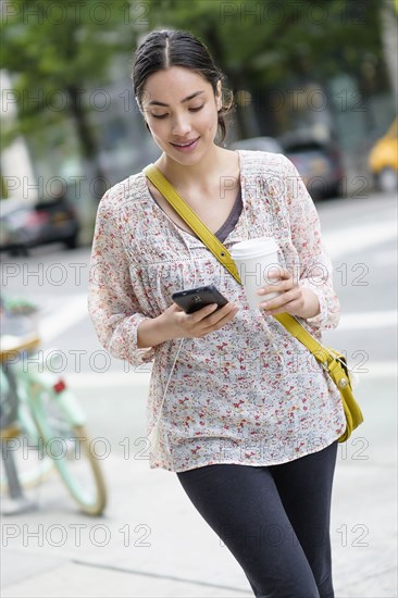 Hispanic woman using cell phone on city sidewalk