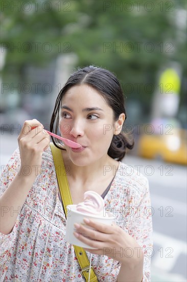 Hispanic woman eating frozen yogurt on city sidewalk