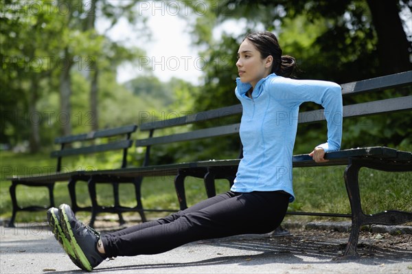 Hispanic woman doing push-ups on park bench