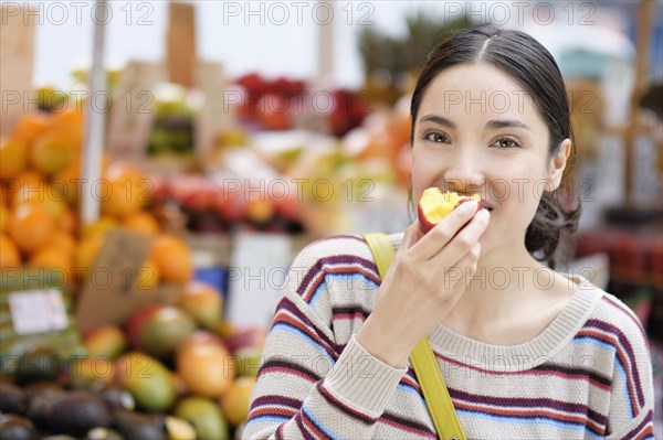 Hispanic woman eating fruit at farmers market