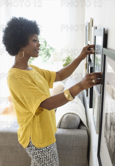 African American woman hanging pictures on living room wall