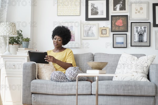 African American woman using digital tablet on sofa