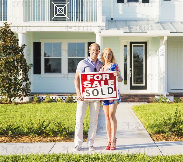 Caucasian couple holding sold sign outside new home