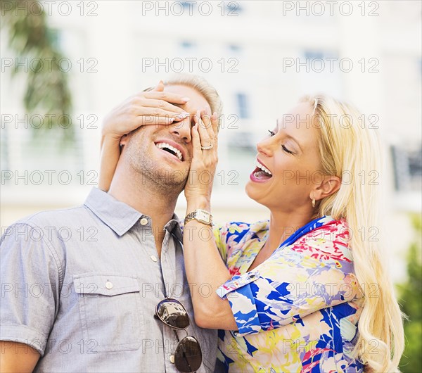 Caucasian woman covering eyes of husband