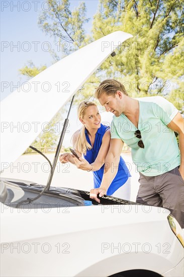 Caucasian couple examining broken down car