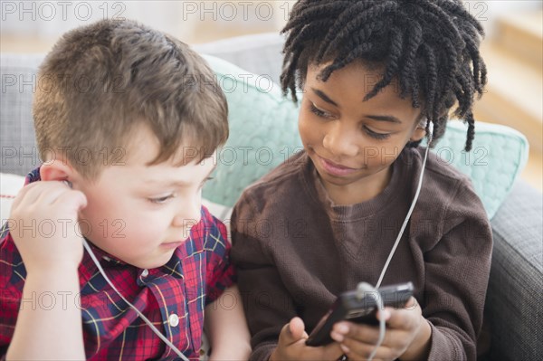 Boys sharing headphones and cell phone on sofa