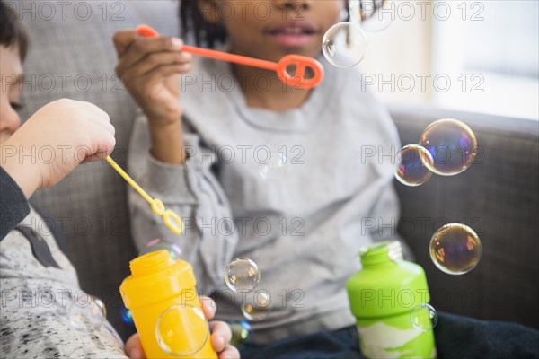Close up of boys blowing bubbles on sofa