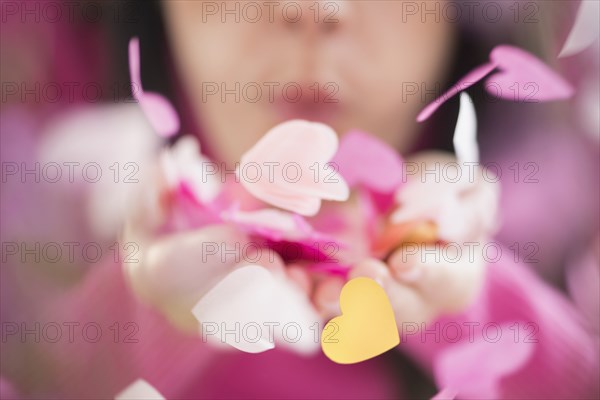 Mixed race woman blowing confetti hearts