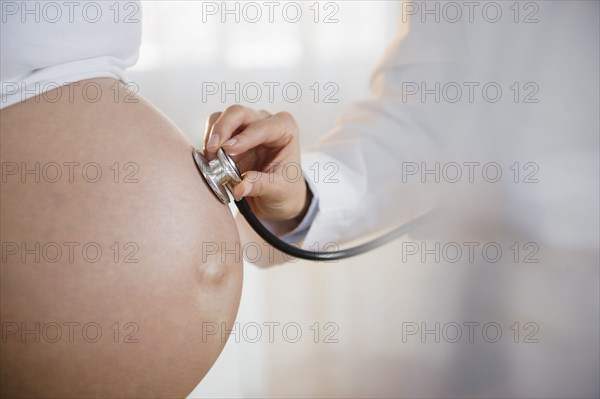 Doctor listening to belly of pregnant woman with stethoscope