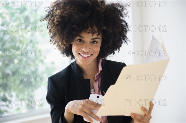 Mixed race businesswoman using cell phone near window