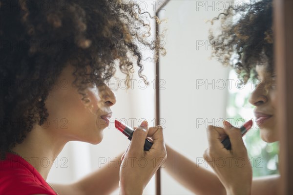 Mixed race woman applying lipstick in mirror