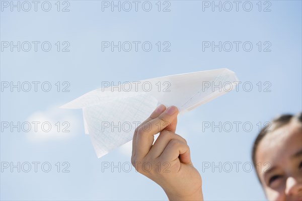 Girl holding paper airplane under blue sky