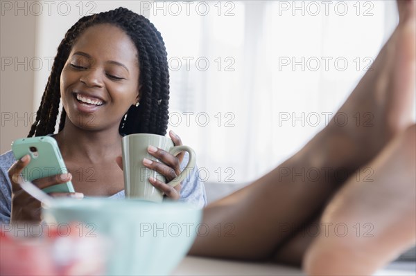 Black woman using cell phone and drinking coffee