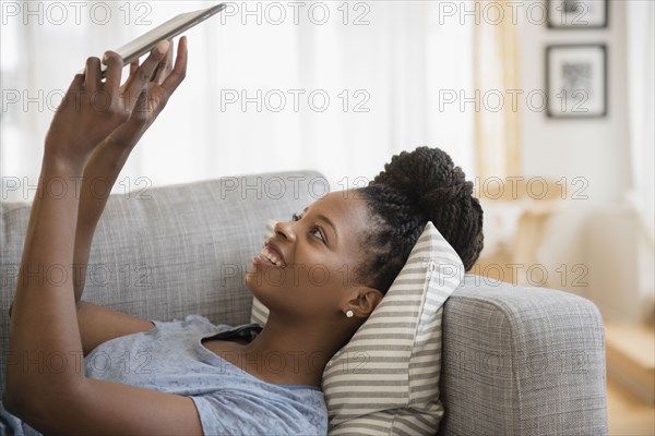 Black woman using digital tablet on sofa