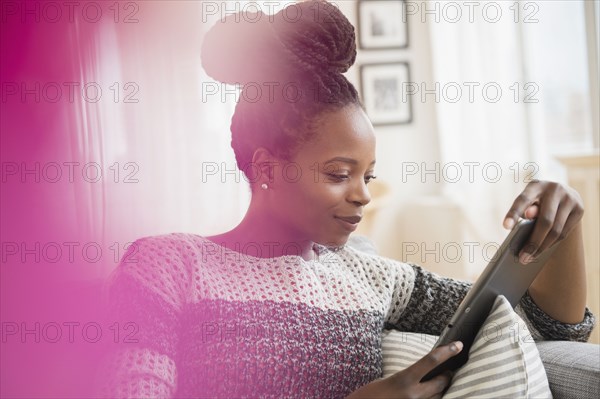 Black woman using digital tablet on sofa