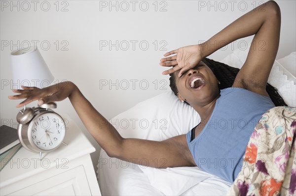 Black woman waking up with alarm clock