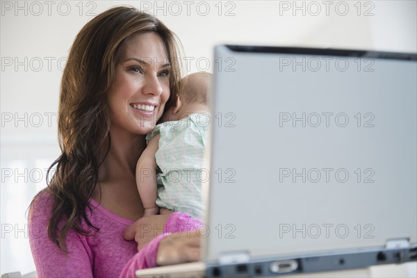 Mother using laptop and holding baby daughter