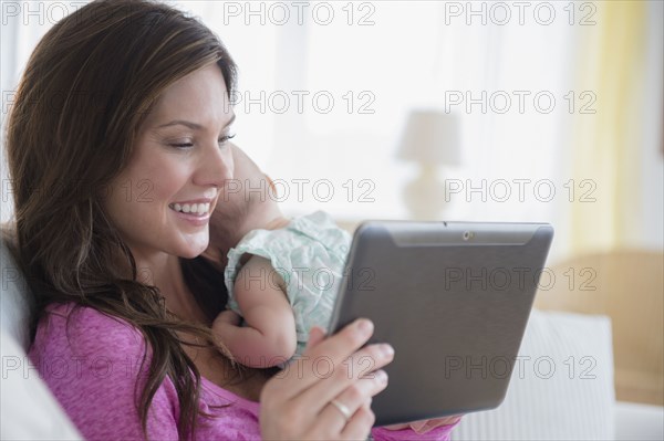 Mother using digital tablet and holding baby daughter