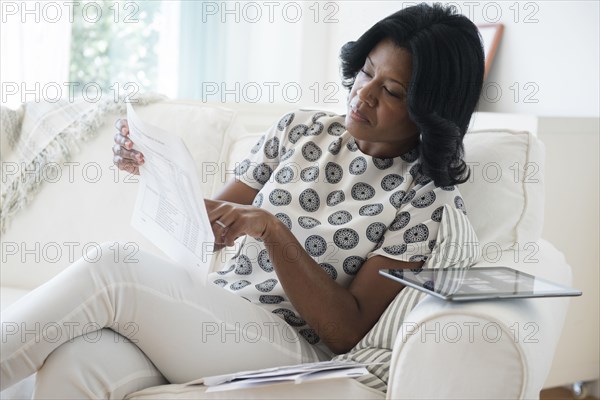 Black woman reading bills on sofa