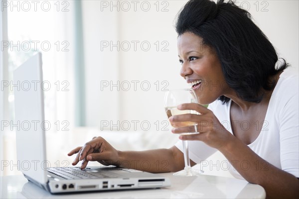 Black woman drinking wine and using laptop