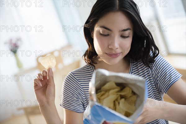 Hispanic woman reading ingredients on bag of potato chips