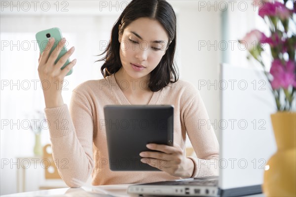 Hispanic woman using cell phone and digital tablet