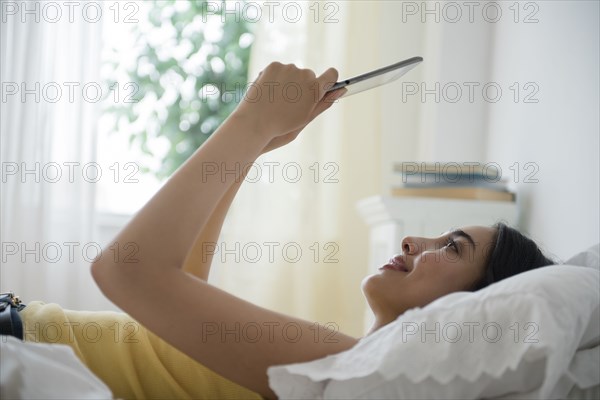 Hispanic woman using digital tablet in bed