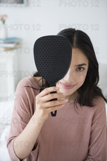 Hispanic woman peeking out from behind hand mirror