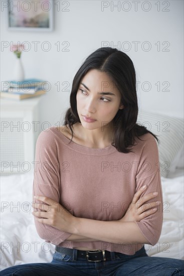 Frustrated Hispanic woman sitting on bed