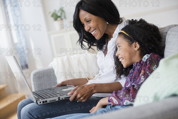 Mother and daughter using laptop on sofa