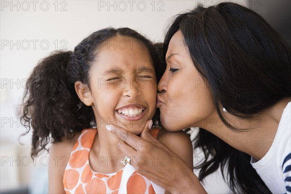 Mother kissing cheek of squinting daughter