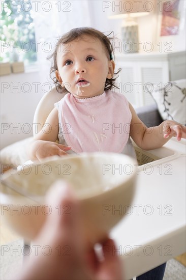 Mother feeding baby daughter in high chair