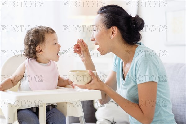 Mother feeding baby daughter in high chair