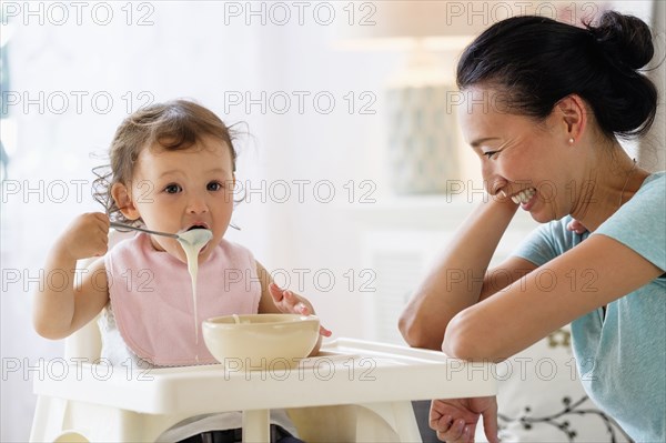Mother watching baby daughter eat in high chair