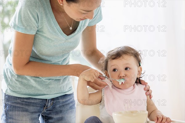 Mother feeding baby daughter in high chair