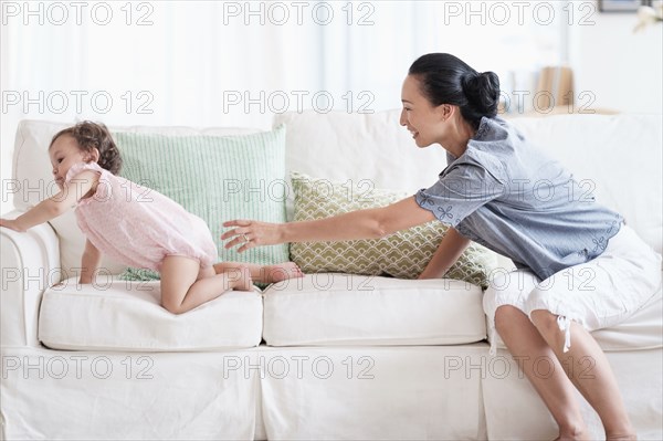 Mother and baby daughter playing on sofa