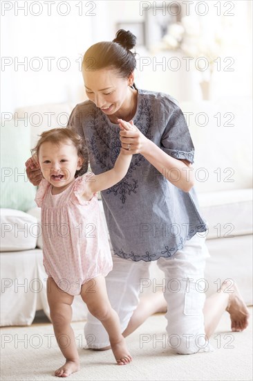 Mother helping baby daughter walk in living room