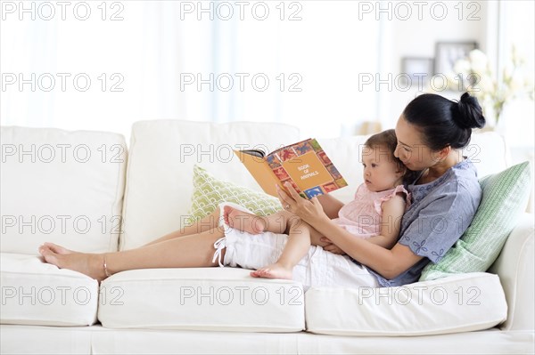 Mother and baby daughter reading on sofa