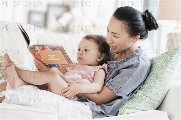 Mother and baby daughter reading on sofa