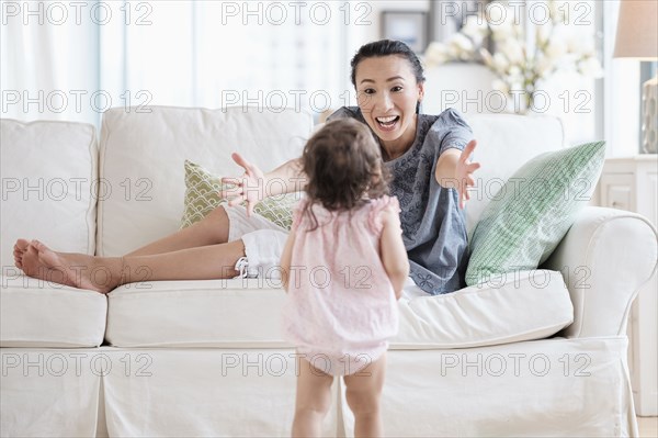 Mother reaching for baby daughter on sofa