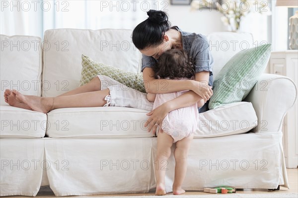 Mother hugging baby daughter on sofa