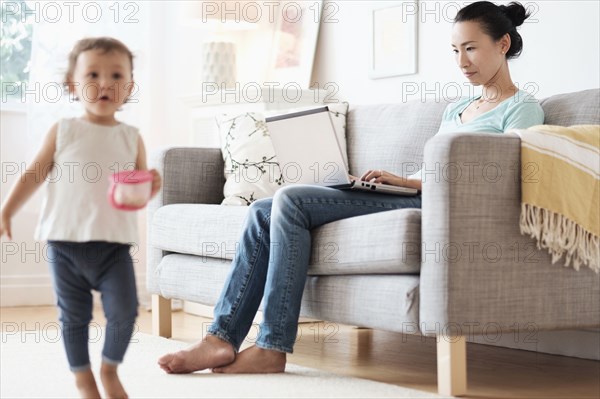 Mother using laptop ignoring baby daughter
