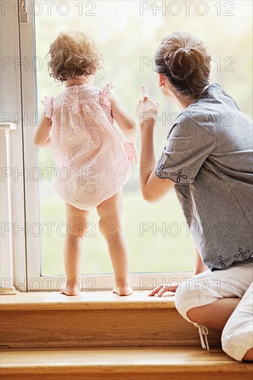 Mother and baby daughter looking out window