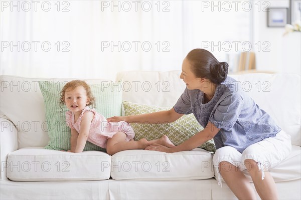Mother and baby daughter playing on sofa