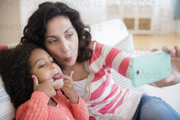 Mother and daughter taking selfie on sofa