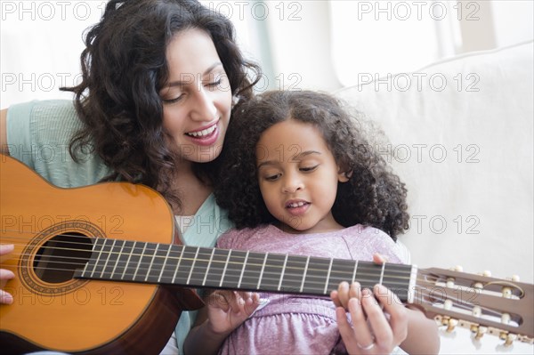 Mother teaching daughter to play guitar